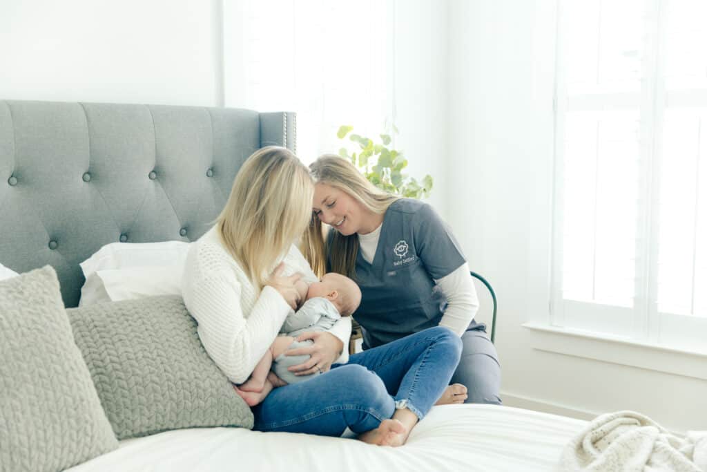 A woman breastfeeding a baby while a lactation consultant helps. 