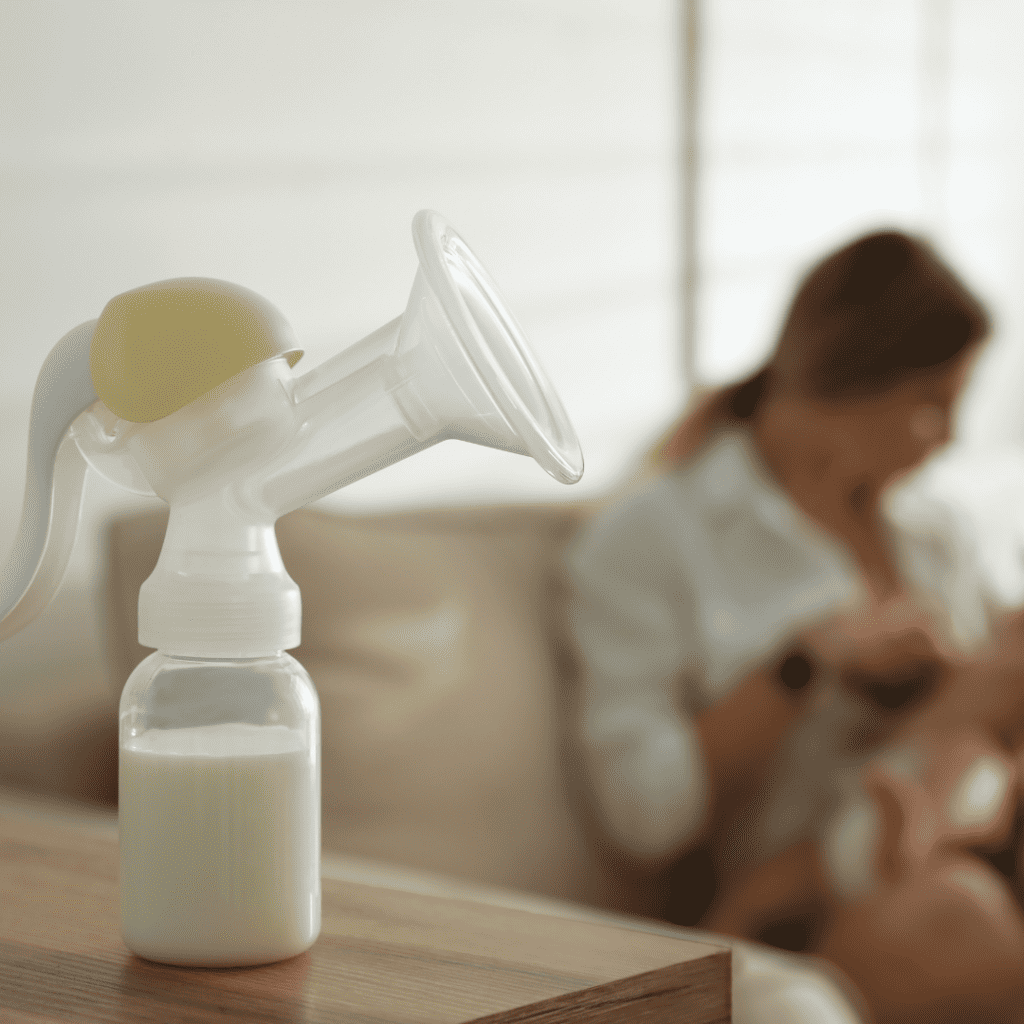 A breast pump with milk and a woman breastfeeding in the background.