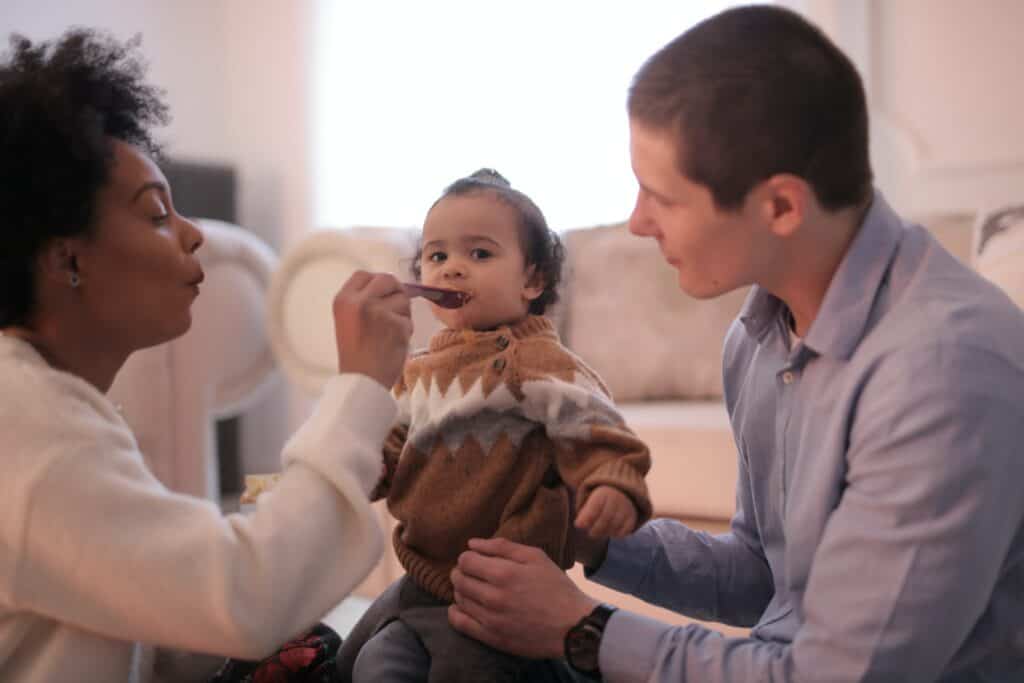 Introducing solids to baby Man holding baby while woman spoons food