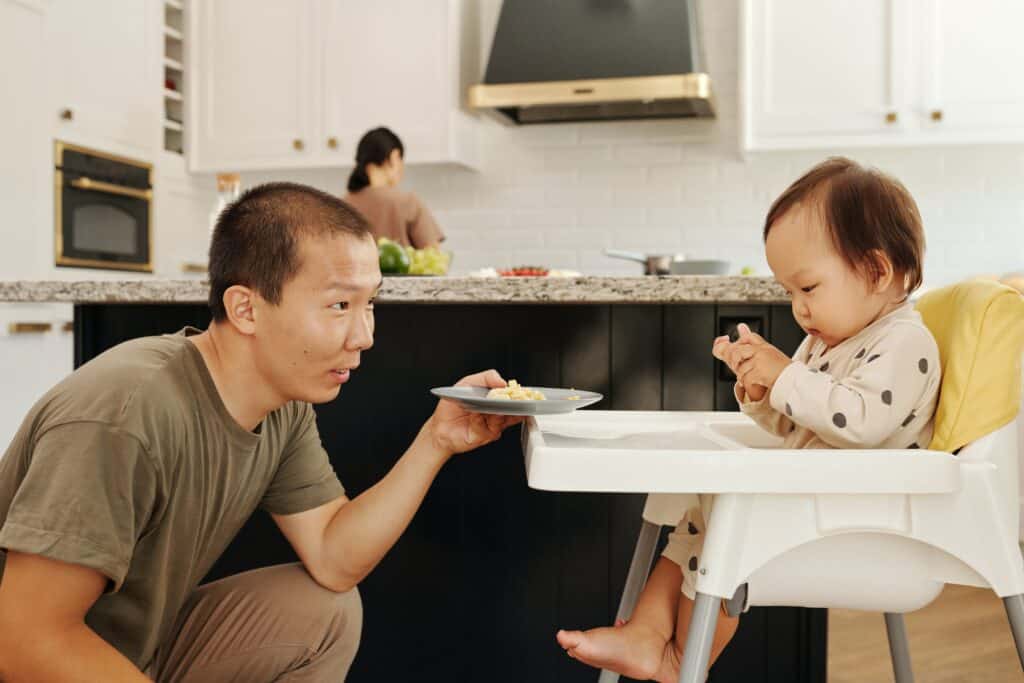 Man offering plate of food to baby in highchair 