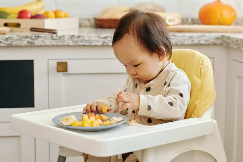 Introducing solids to baby Baby in highchair with plate of cut up fruit