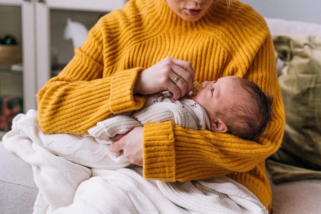 Woman holding baby and putting pacifier into their mouth