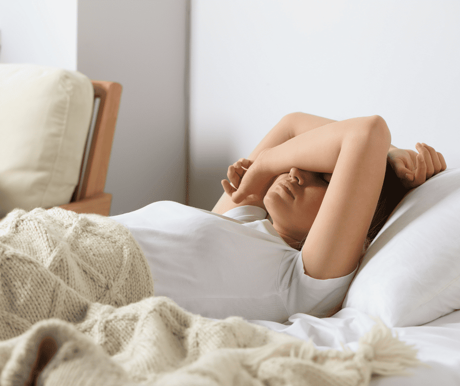Woman laying in bed with arms over her face 