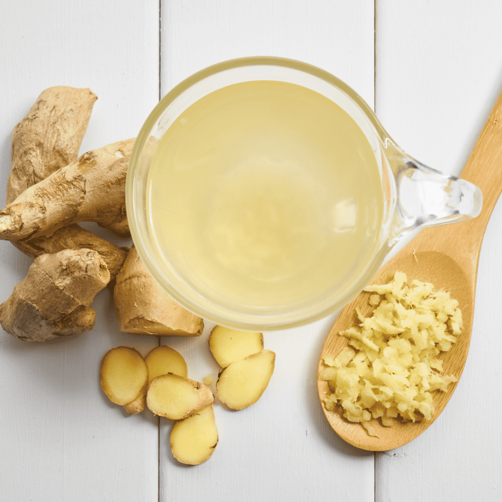 A cup of ginger tea with cut up ginger, minced ginger, and whole ginger around it