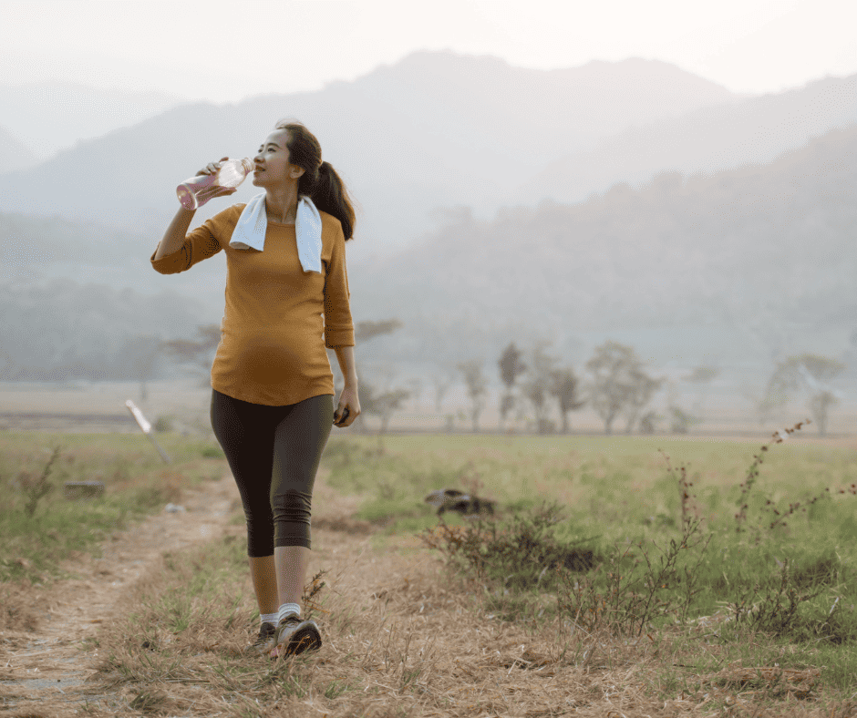 Pregnancy safe exercises Pregnant woman walking on nature path drinking a bottle of water