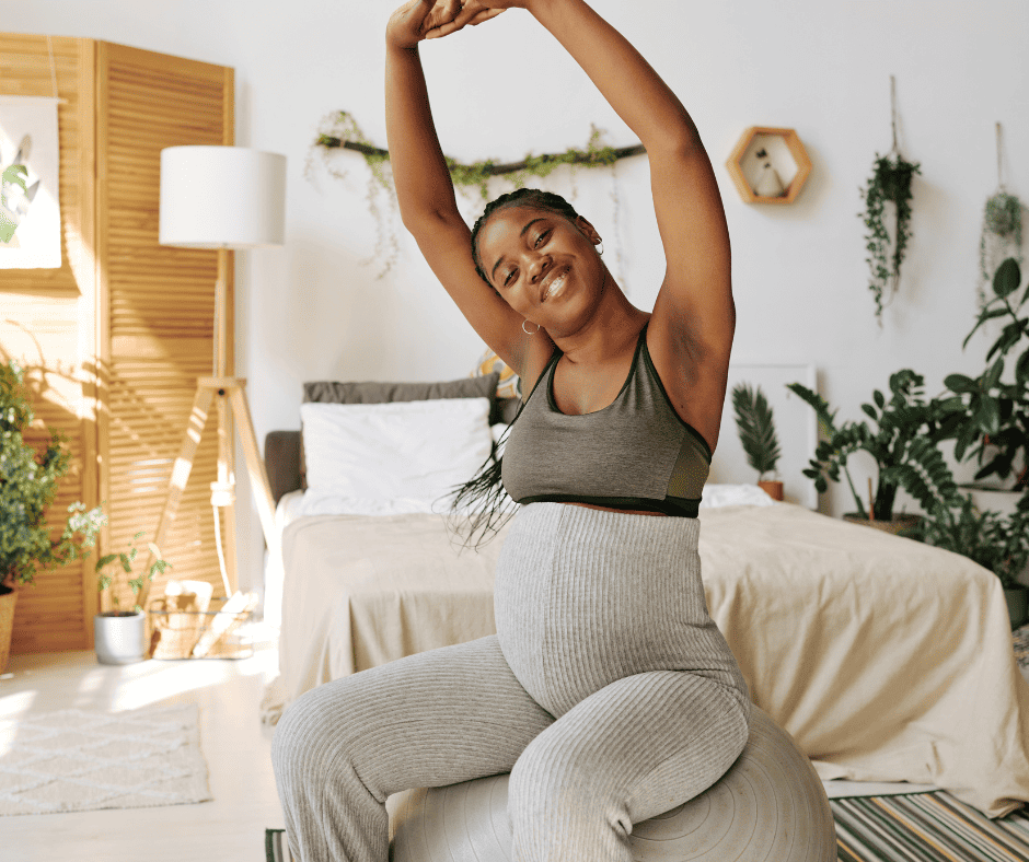 Pregnant woman on exercise ball stretching her arms up. 