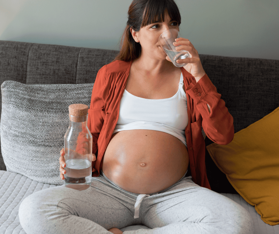 Pregnant woman drinking water while sitting on couch