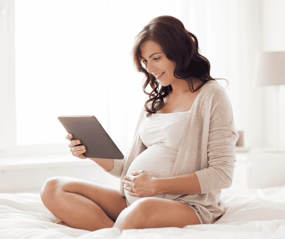 Pregnant woman sitting cross legged on bed looking at iPad