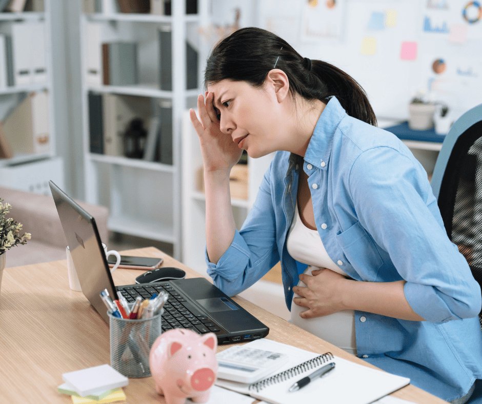 Pregnant woman at desk with laptop looking stressed