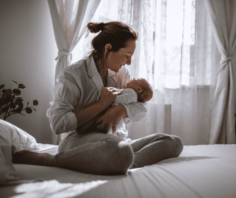 Woman holding baby while sitting on bed