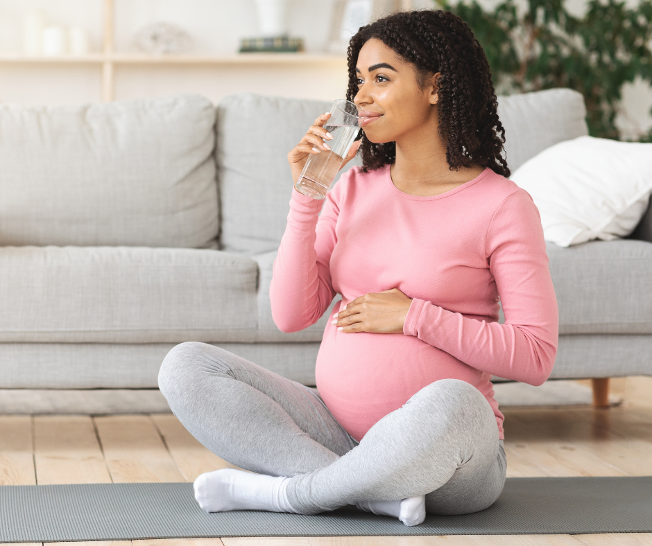 Pregnant woman sitting on yoga mat drinking a glass of water