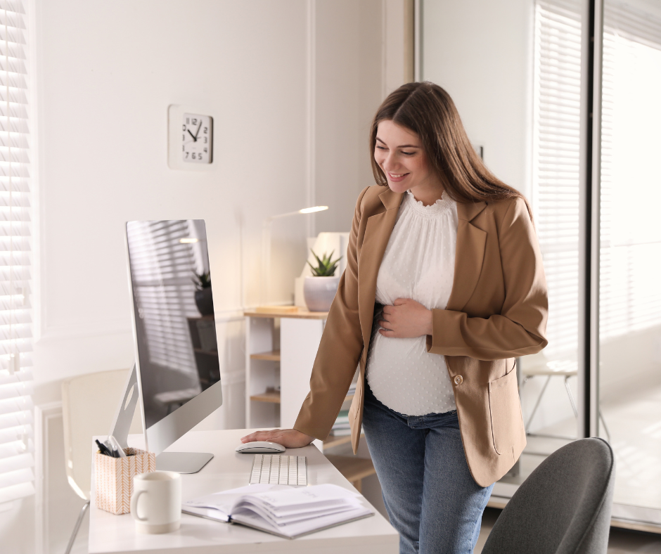 Pregnant woman standing by desk with computer